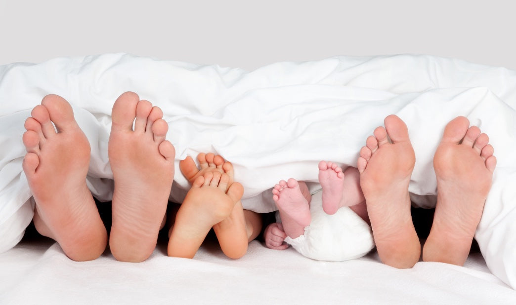 family sleeping in bed under white comforter