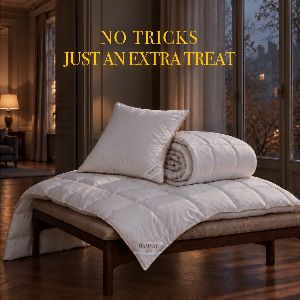 A white quilted bedding set, including a duvet cover and matching pillow, styled on a wooden daybed in a luxurious, warmly lit bedroom. The text 'NO TRICKS JUST AN EXTRA TREAT' is displayed at the top.