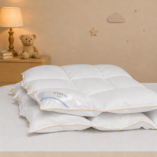 A Hamvay-Láng comforter for kids with light beige piping, displayed on a bed in a softly lit bedroom setting with a bedside lamp and teddy bear.