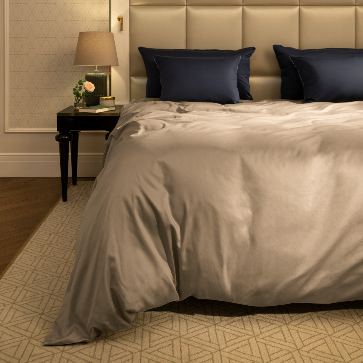Neatly made bed with beige bedding and navy pillows in a bedroom setting.