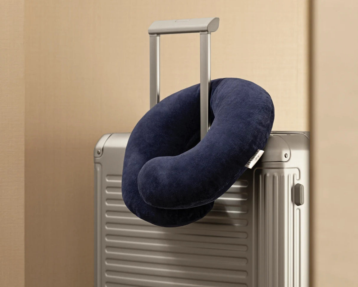 Navy blue travel neck pillow on a silver suitcase against a beige background