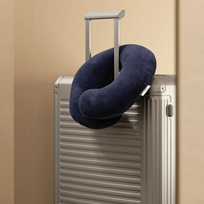 Navy blue travel neck pillow on a silver suitcase against a beige background