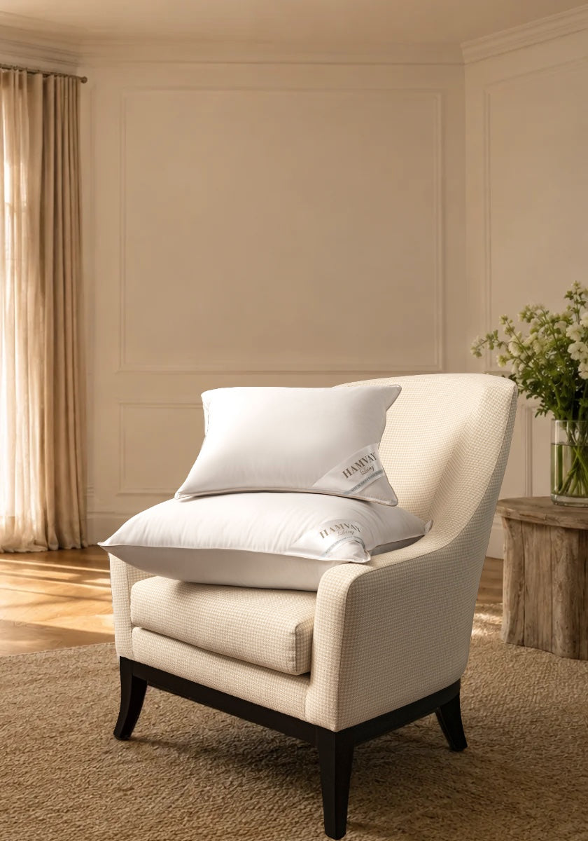 A cream upholstered armchair in a warm neutral room, styled with two white pillows. 